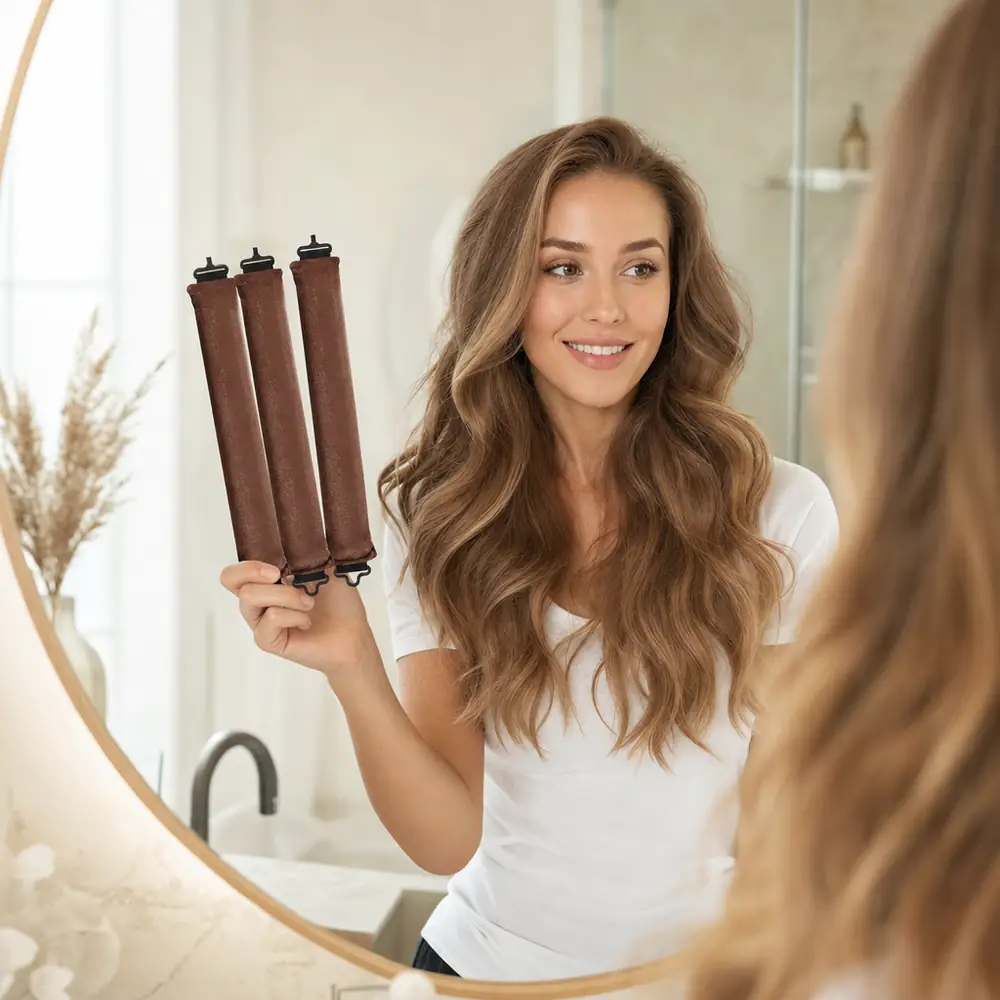 Smiling woman with long brown waves at a mirror, holding three coffee heatless curling rods