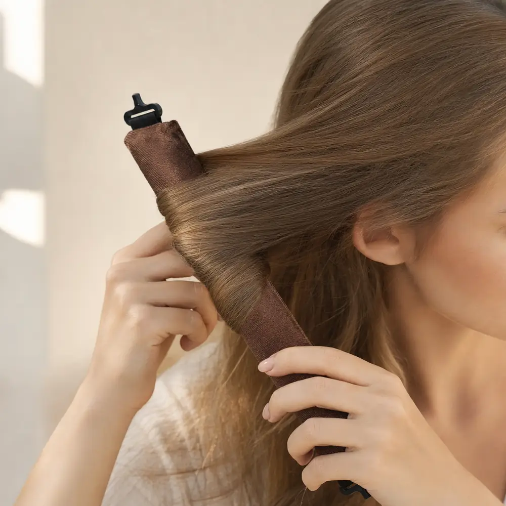 Hands wrapping a section of long light-brown hair in a spiral around a coffee velvet-soft rod held upright